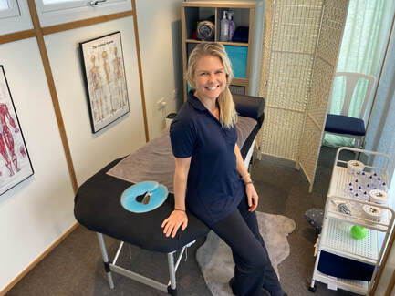 Georgina sitting on the edge of the treatment couch in the BodyFix treatment room, anatomy charts on the wall behind her